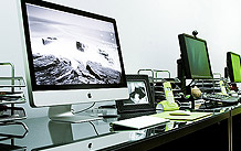 Imagen de los puestos de trabajo. iMac de 27 pulgadas y otros equipos Windows con pantallas Dell de 24 pulgadas sobre mesas negras.
